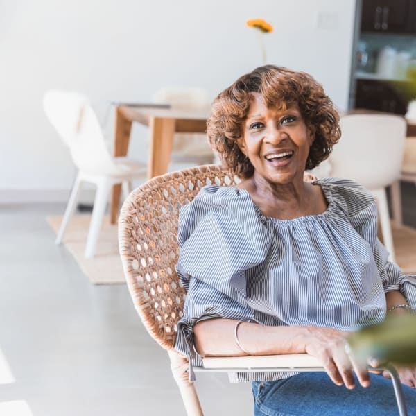 Resident sitting in a chair and smiling at Pacifica Senior Living Menifee in Sun City, California.