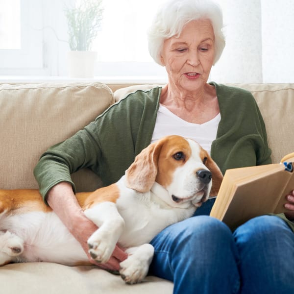 Resident snuggling with a dog and reading at Pacifica Senior Living Sterling in Sterling, Virginia