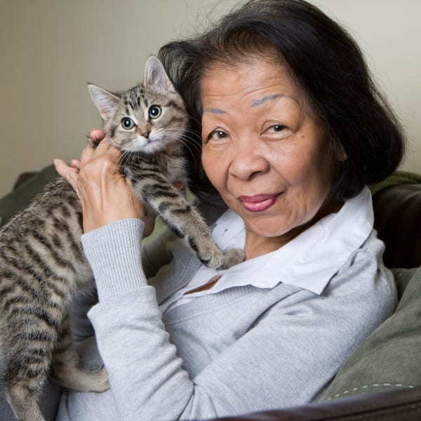 Resident smiling and posing with striped tabby cat at Pacifica Senior Living Santa Rosa in Santa Rosa, California
