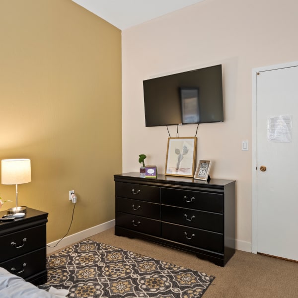 Resident bedroom with end table, dresser, and large tv at Pacifica Senior Living Burlingame in Burlingame, California