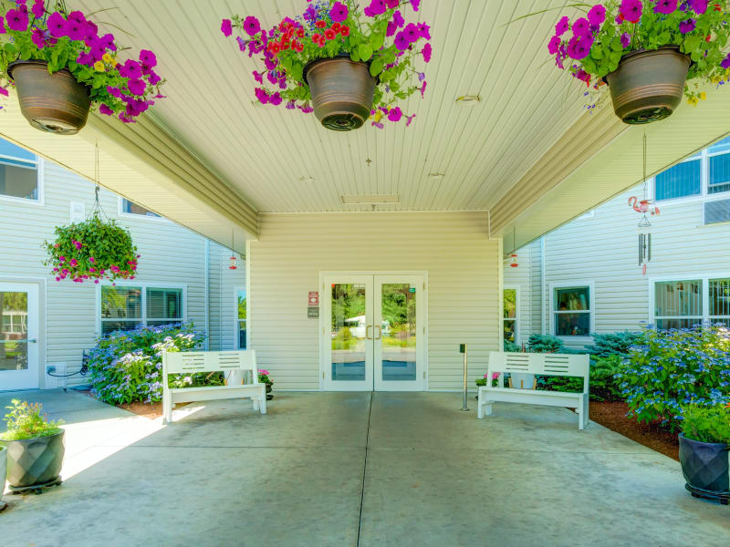 Covered entrance to The Suites Assisted Living and Memory Care with hanging flower baskets and benches in Grants Pass, Oregon