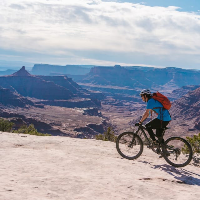 StorQuest Self Storage ambassador Kyle Frost mountain biking on a ridge above a desert canyon