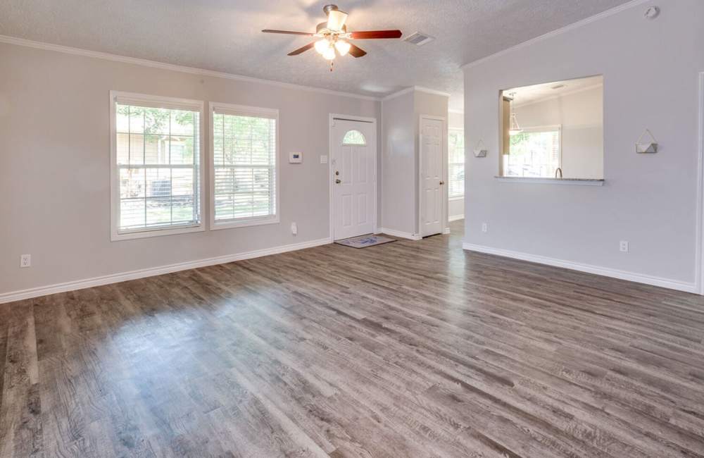 Living room with hard wood flooring and two window at Waterstone Place Apartments in Stafford, Texas