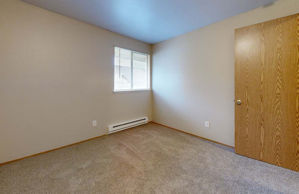 An empty carpeted bedroom with a window at Heron Hills Apartment Homes in Gresham, Oregon