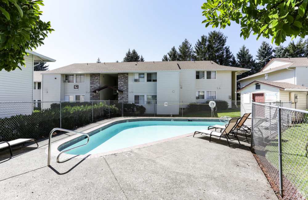 A fenced-in outdoor swimming pool with several lounge chairs at Heron Hills Apartment Homes in Gresham, Oregon