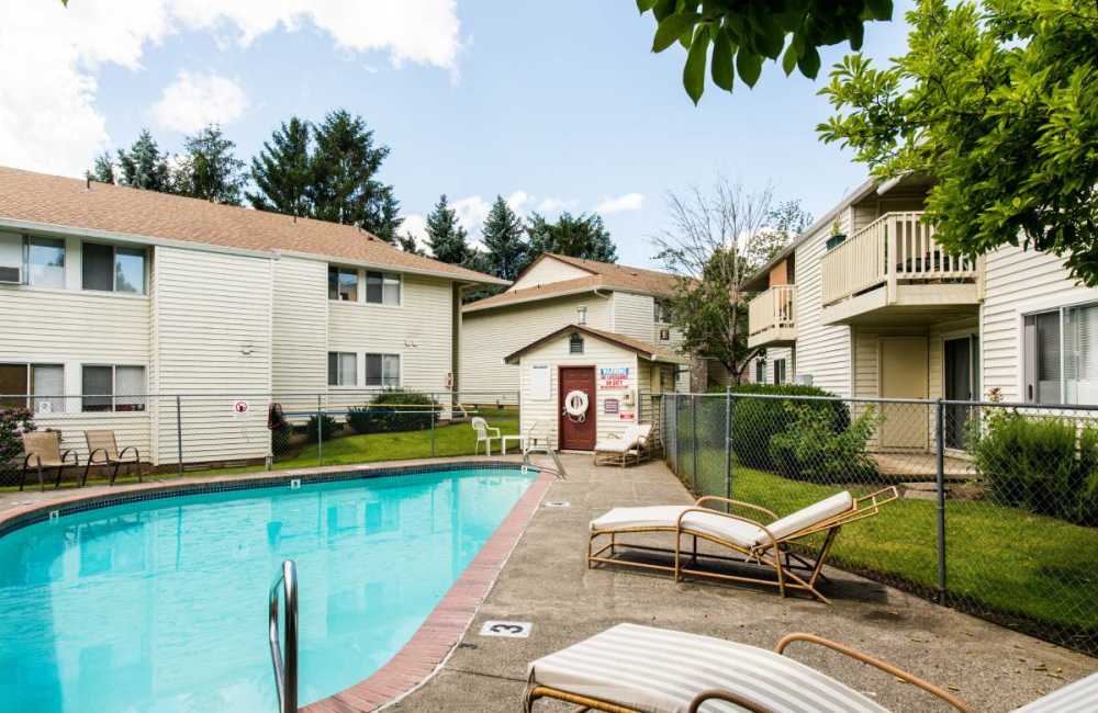 Swimming pool surrounded by a metal fence, two lounge chairs and buildings at Heron Hills Apartment Homes in Gresham, Oregon