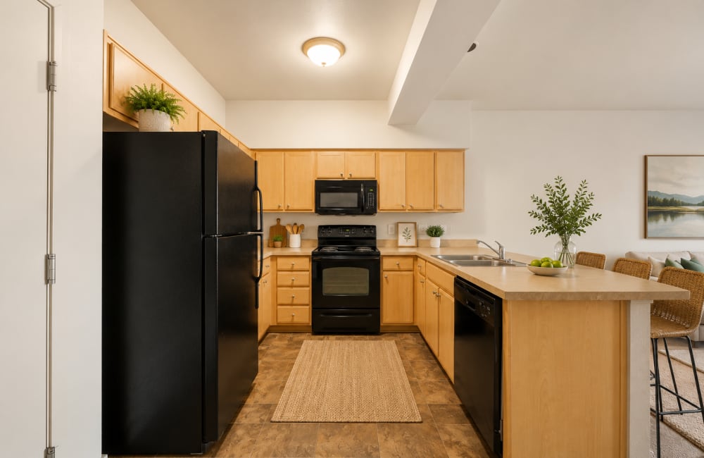 Compact kitchen with wood cabinets, black refrigerator, stove, and microwave at North Main Village in Milwaukie, Oregon