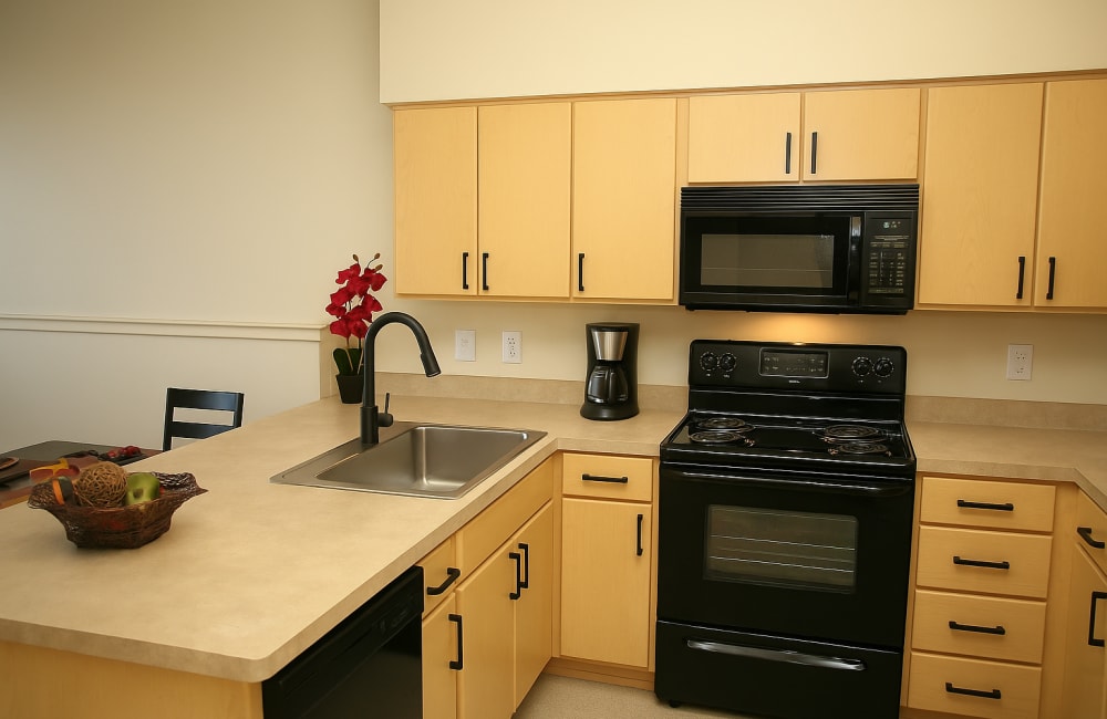 Modern kitchen with island sink, wood cabinetry, black stove, and microwave at North Main Village in Milwaukie, Oregon