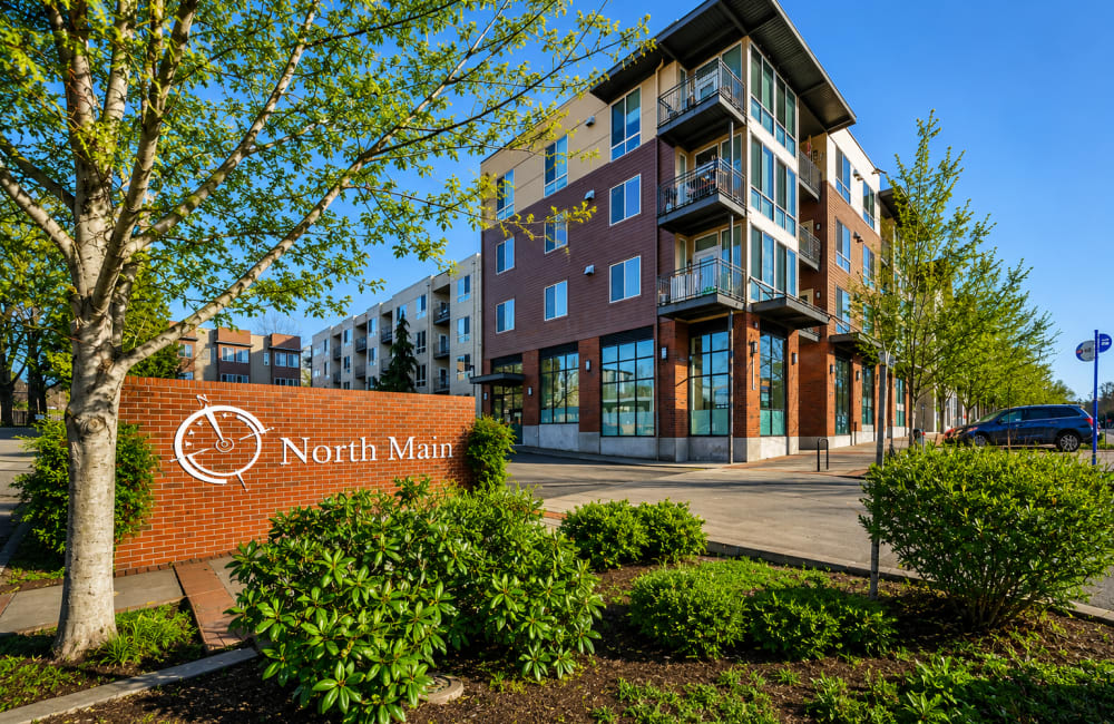 Modern apartment complex with parking lot and trees along a quiet street at North Main Village in Milwaukie, Oregon
