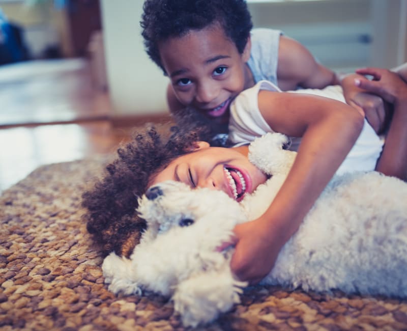 Two little kids snuggling with their dog on the floor at Branchwood Apartments in Winter Park, Florida