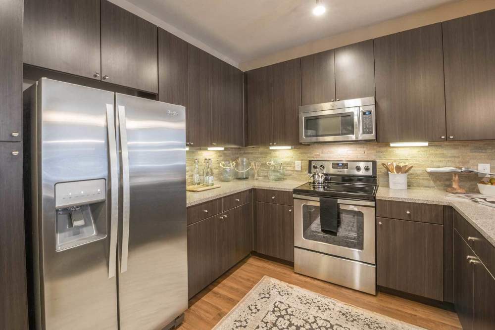 Fully-equipped kitchen with stainless steel appliances and island with bar stools and wood cabinetry at The Abbey at Spring Town Center in Spring, Texas