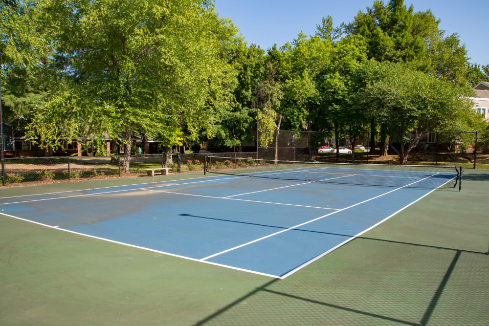 A tennis court surrounded by large deciduous trees at Sunbrook Apartments in Saint Charles, Missouri