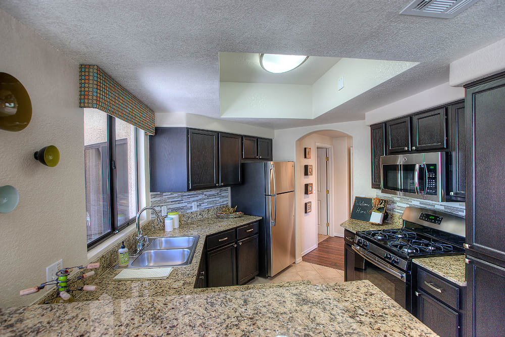 Gourmet kitchen with granite countertops and dark wood cabinetry in a model home at San Pedregal in Phoenix, Arizona