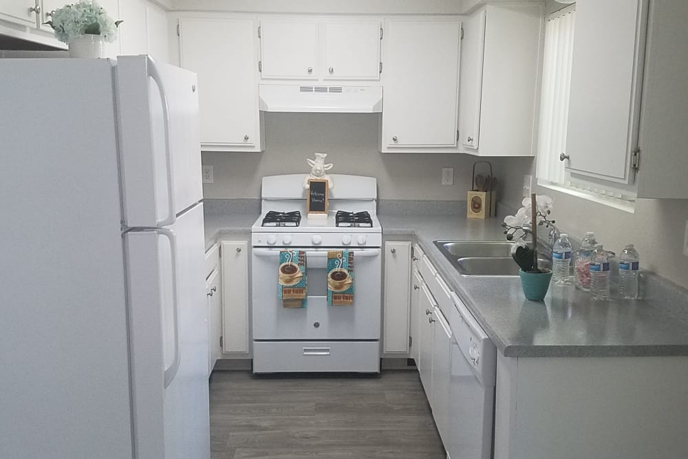 Modern kitchen with granite countertops and white appliances in model home at Sienna Heights Apartment Homes in Lancaster, California