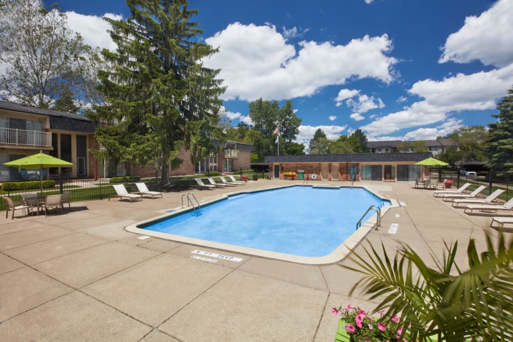 Swimming pool surrounded by lounge chairs and umbrellas at Kensington Manor Apartments in Farmington, Michigan