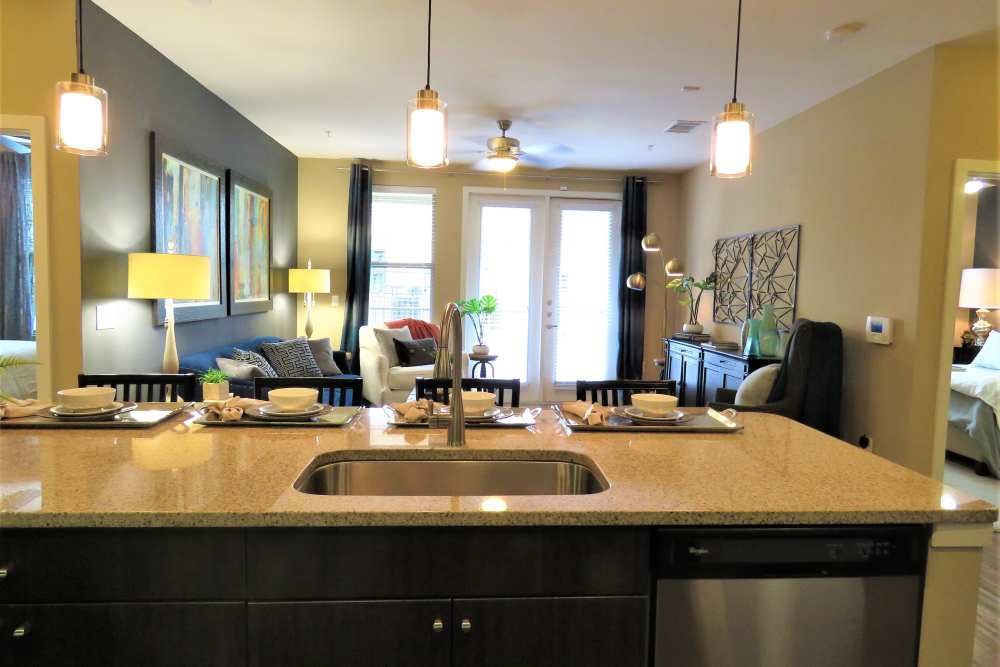 View of living room from kitchen island with stainless steel sink with waterfall faucet and pendant lighting at The Abbey at Spring Town Center in Spring, Texas