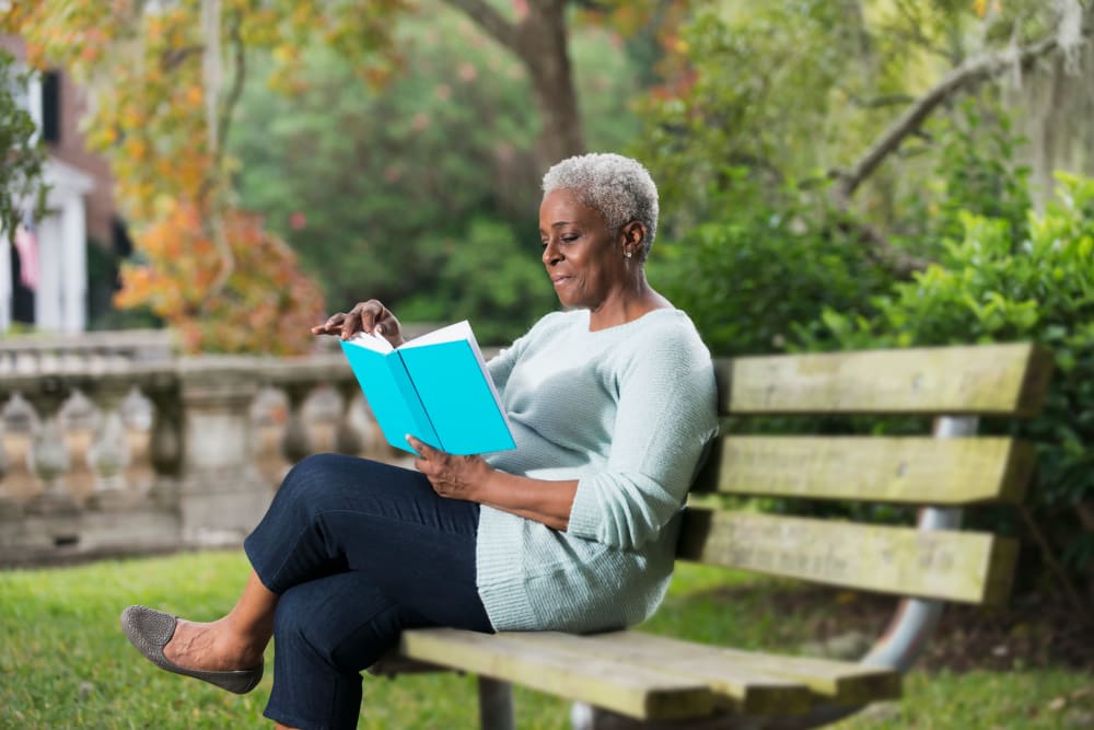 Resident relaxing and reading a book on a bench at a park near WellQuest of Elk Grove in Elk Grove, California
