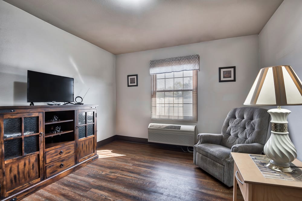 Senior apartment living room with a tv, cooling unit, and darkwood furniture at Oak Pointe of Warrenton in Warrenton, Missouri