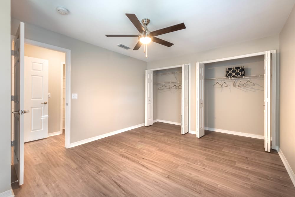 Hardwood flooring, a ceiling fan, and ample closet space in a model apartment's bedroom at Cape House in Jacksonville, Florida