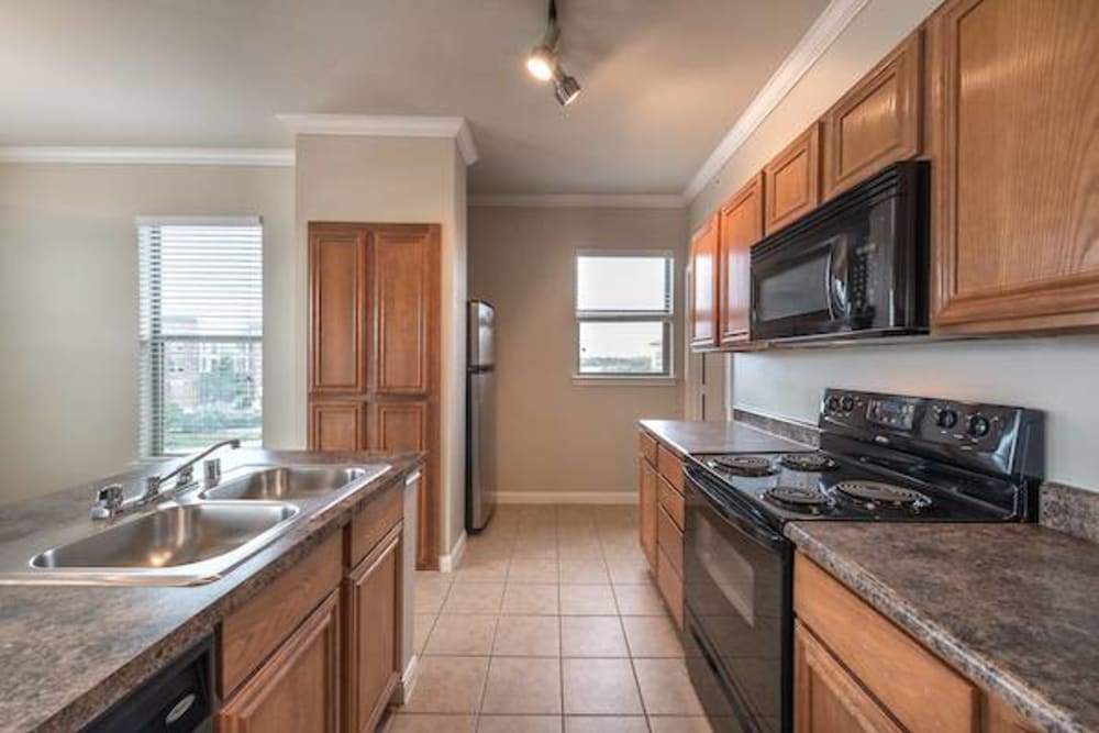 Cherry wood cabinetry and black appliances in a model home's kitchen at Olympus Las Colinas in Irving, Texas