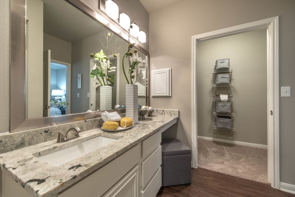 Primary bathroom with a granite countertop and hardwood flooring in a model home at Olympus Las Colinas in Irving, Texas
