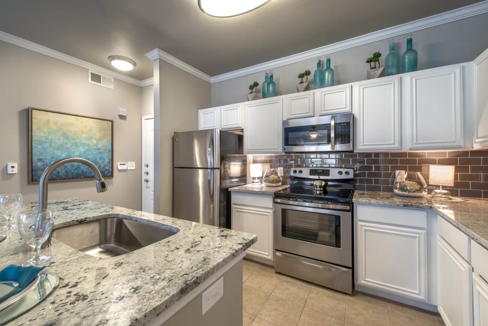 Model apartment kitchen with stainless-steel appliances and white cabinetry at Olympus Las Colinas in Irving, Texas