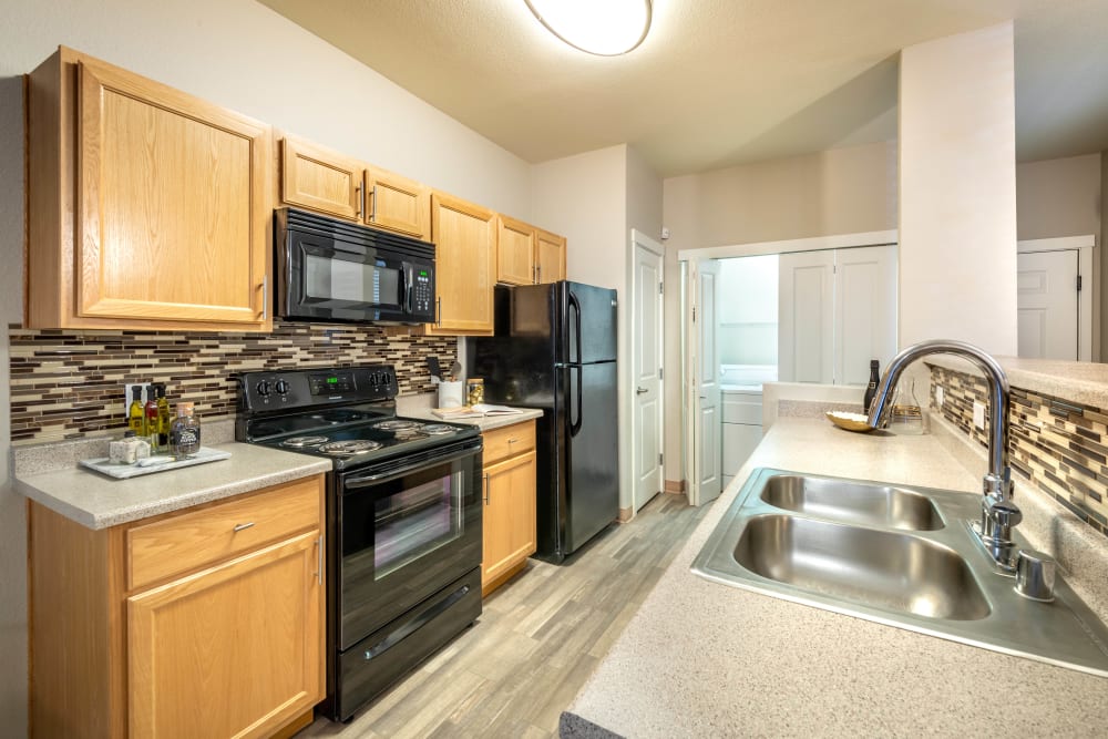 Sleek black appliances and a custom tile backsplash in a model home's kitchen at Olympus Solaire in Albuquerque, New Mexico