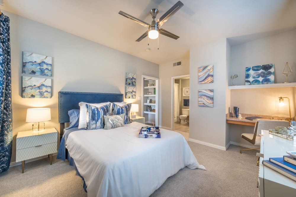 Model home's spacious primary bedroom with a ceiling fan and classic furnishings at Olympus Stone Glen in Keller, Texas