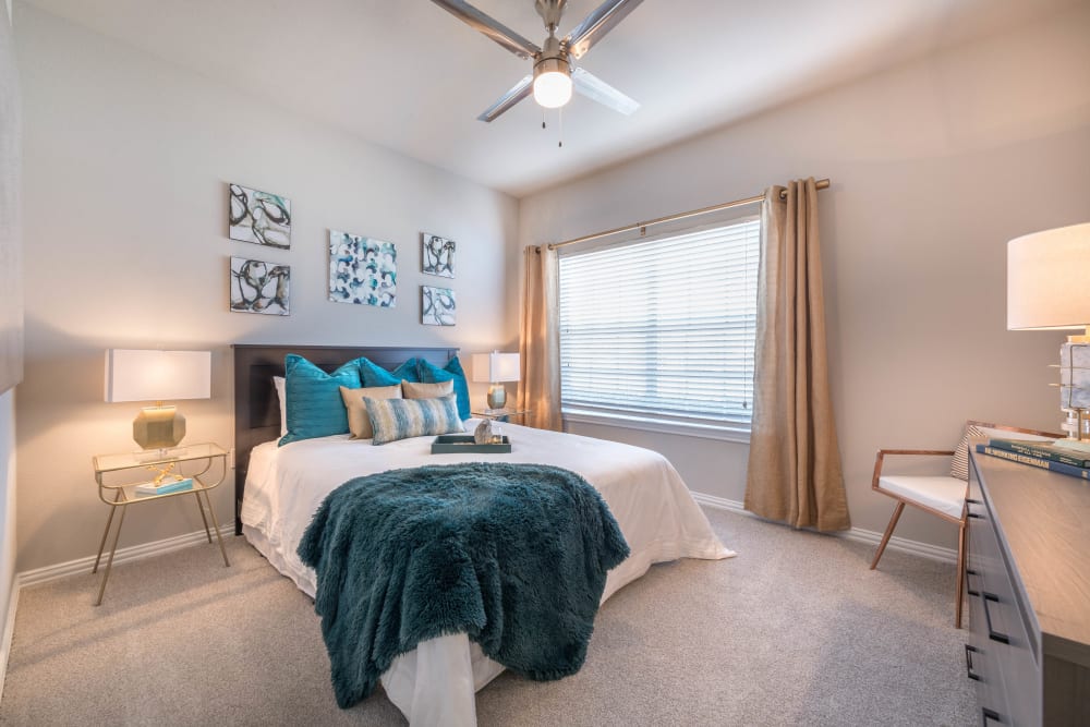 Plush carpeting and a ceiling fan in the spacious primary bedroom of a model apartment at Olympus Stone Glen in Keller, Texas