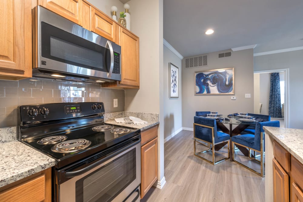 Gourmet kitchen with granite countertops looking into the dining area of a model apartment at Olympus Stone Glen in Keller, Texas