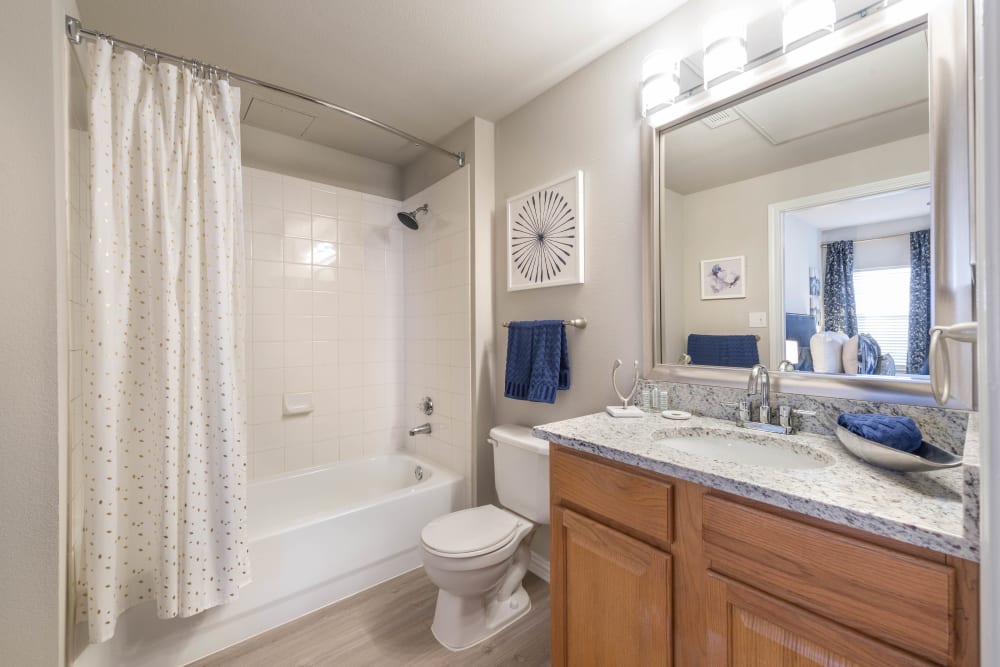 Primary bathroom with a large vanity mirror and a tiled shower in a model apartment at Olympus Stone Glen in Keller, Texas