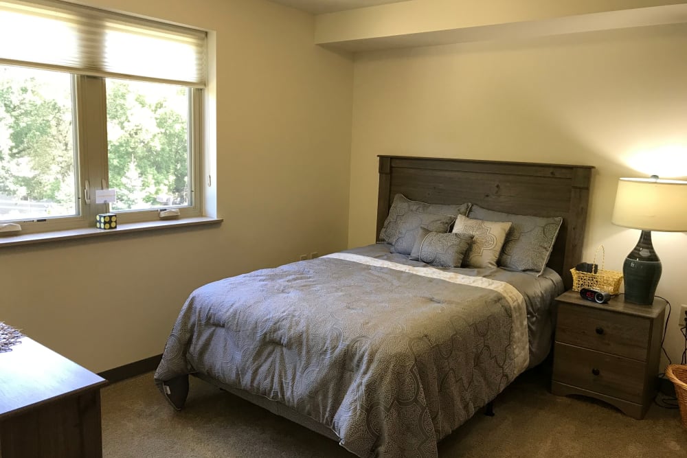 Resident bedroom with a side table at Prairie Hills Cedar Rapids in Cedar Rapids, Iowa. 