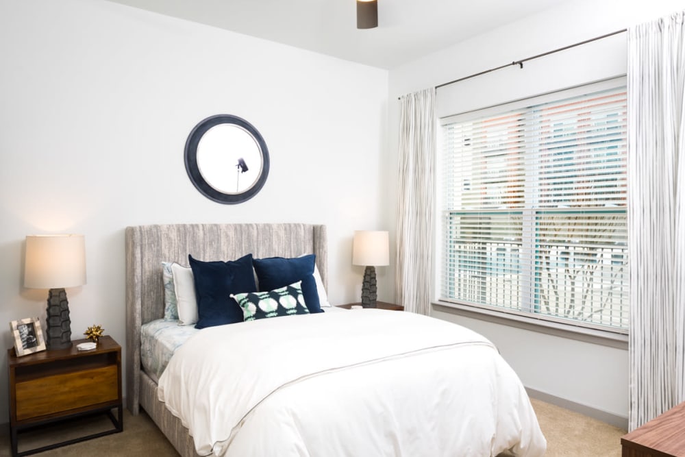 Large bay windows and a ceiling fan in a model apartment's bedroom at Lux on Main in Carrollton, Texas