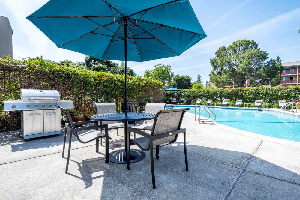 Outdoor pool, patio table with chairs and umbrella at Waterstone Fremont in Fremont, California