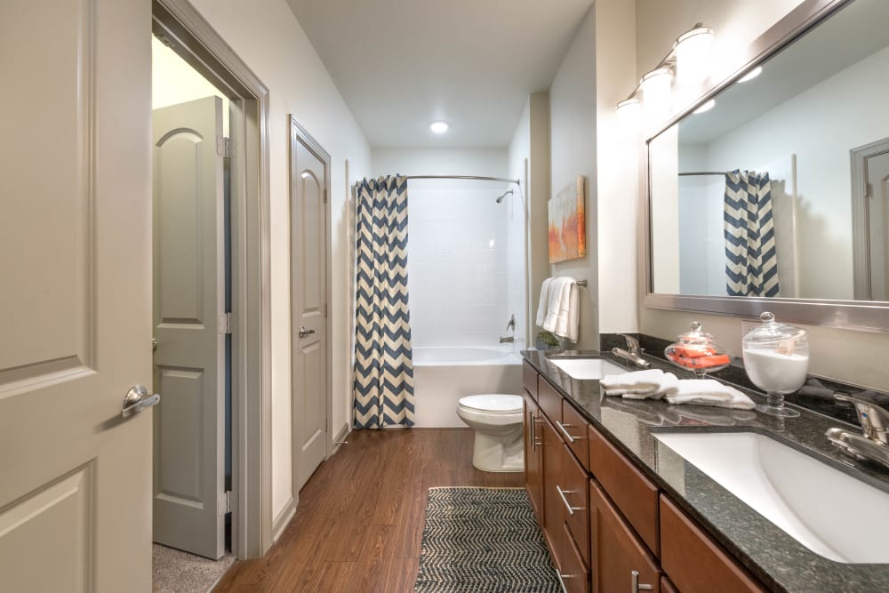 Dual sinks and a granite countertop in a model apartment's bathroom at Olympus Waterford in Keller, Texas