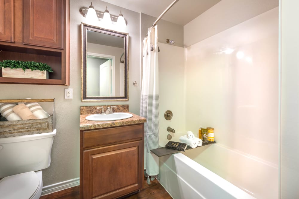 Model home's bathroom with a tiled shower and cherry wood cabinetry at Olympus Willow Park in Willow Park, Texas