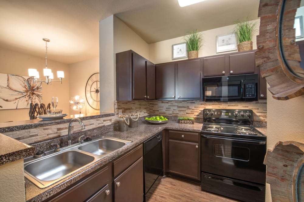 Dark wood cabinetry and sleek black appliances in a model apartment's kitchen at The Ranch at Shadow Lake in Houston, Texas