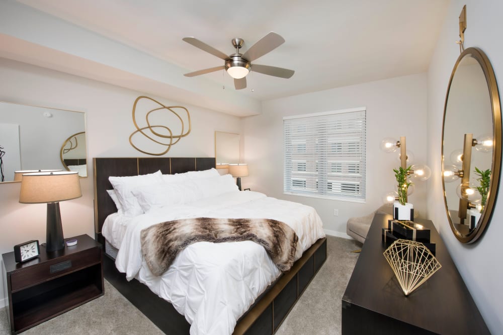 Well-furnished master bedroom with a ceiling fan and plush carpeting in a model apartment at Olympus Harbour Island in Tampa, Florida