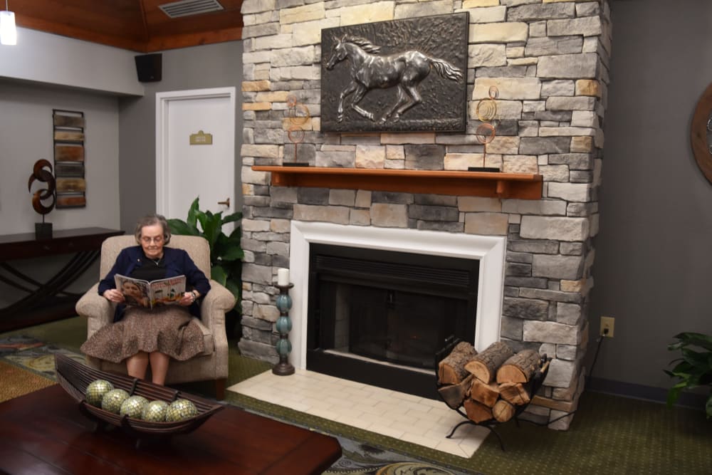Resident relaxes with a magazine by the fireplace at Willow Creek Senior Living in Elizabethtown, Kentucky.