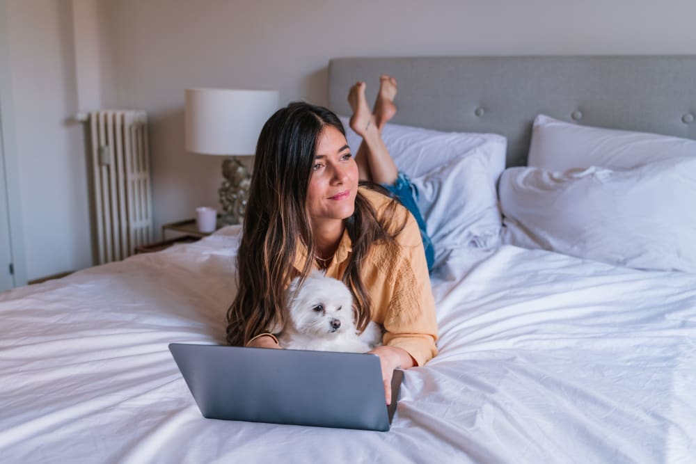 Resident using her laptop in bed with her dog at UNCOMMON Raleigh in Raleigh, North Carolina
