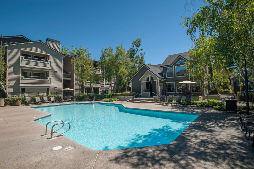 Swimming pool with a large sundeck and lounge chairs at The Reserve at Capital Center Apartment Homes in Rancho Cordova, California