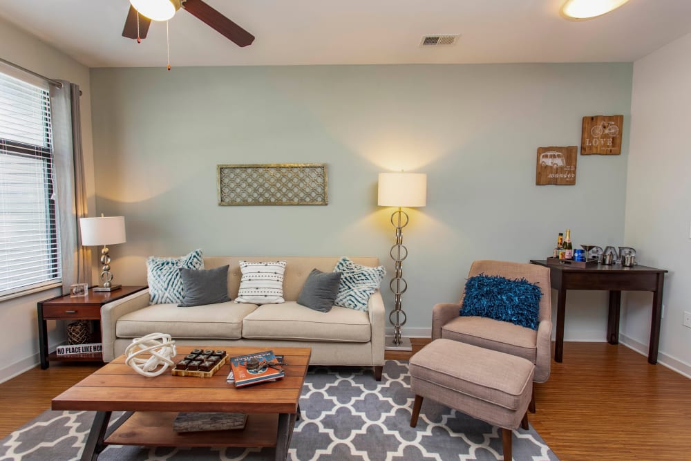 Comfortably furnished living area with an accent wall and hardwood flooring in a model home at Olympus Midtown in Nashville, Tennessee