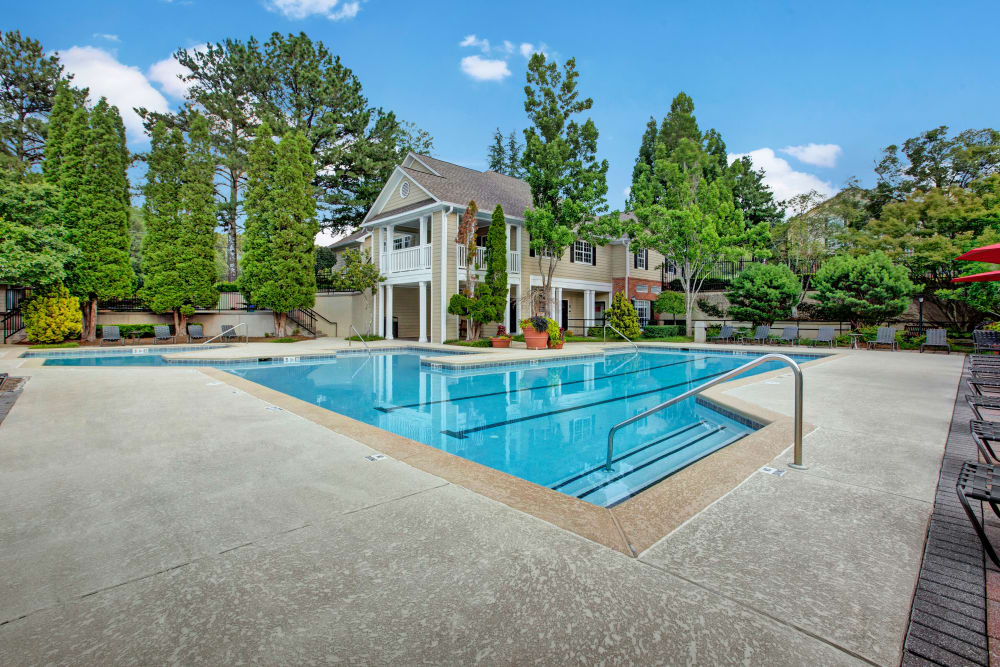 Community pool with mature trees and clubhouse in the background at Avia at North Springs in Atlanta, Georgia 
