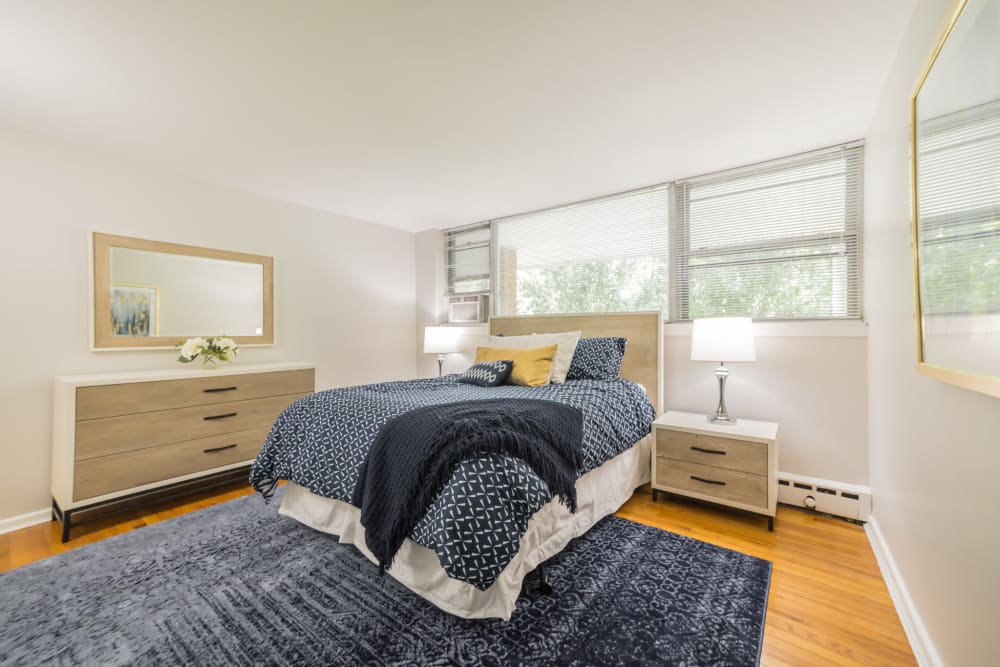 A Spacious bedroom with lots of natural light from large windows pictures comfortable bed and dresser with large vanity mirror in an apartment at Cherokee Apartments in Philadelphia, Pennsylvania