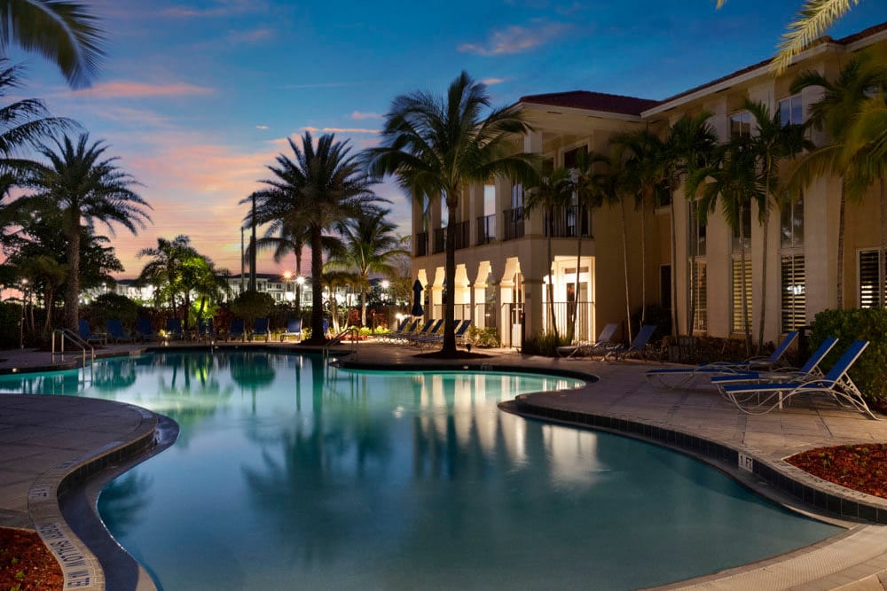 Community pool with palm trees at sunset at City Center on 7th Apartment Homes in Pembroke Pines, Florida