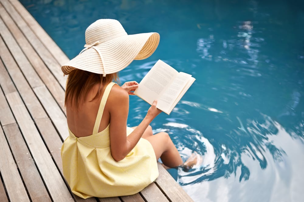 A resident reading a book with her feet in the pool at Artisan Living Bella Citta in Davenport, Florida