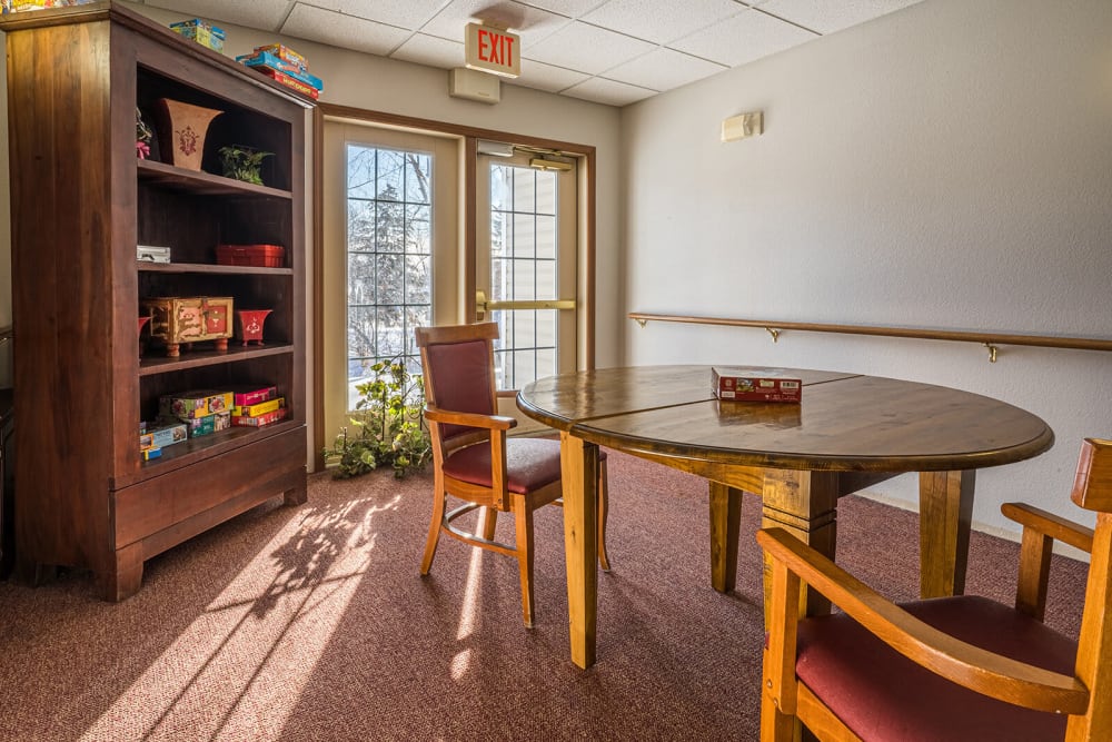 Sunlit game room with a central circular table at Traditions of Owatonna in Owatonna, Minnesota
