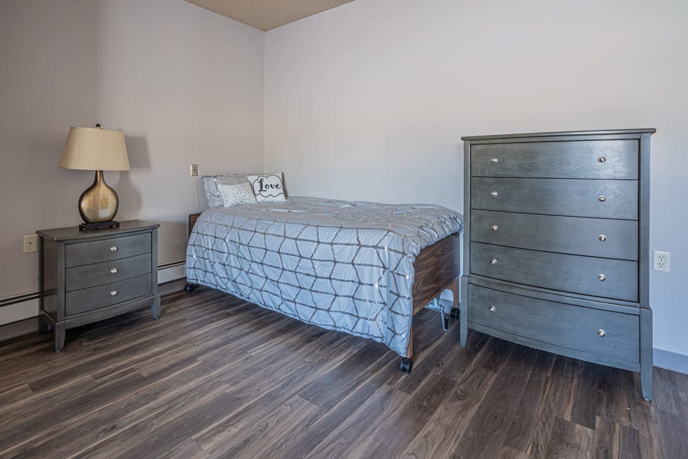 Single person bed next to a nightstand and a dresser at Traditions of Owatonna in Owatonna, Minnesota