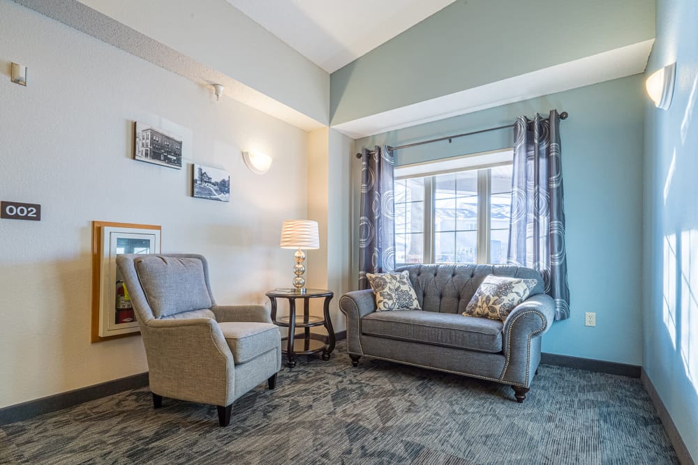 Reading corner with a couch and a chair next to a window at Traditions of Owatonna in Owatonna, Minnesota