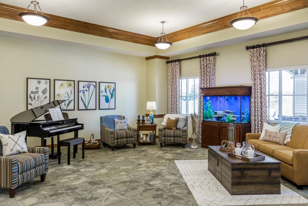 Resident lounge with a bright blue fish tank and a piano at Edencrest at The Legacy in Norwalk, Iowa